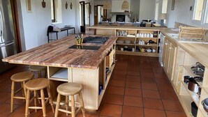 Un'ampia cucina con un'isola grande, sgabelli di legno e un pavimento piastrellato.