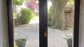 Une porte en bois sombre, dotée de panneaux de verre, qui donne sur un espace recouvert de gravier, agrémenté de plantes en pot et d’un arbre.