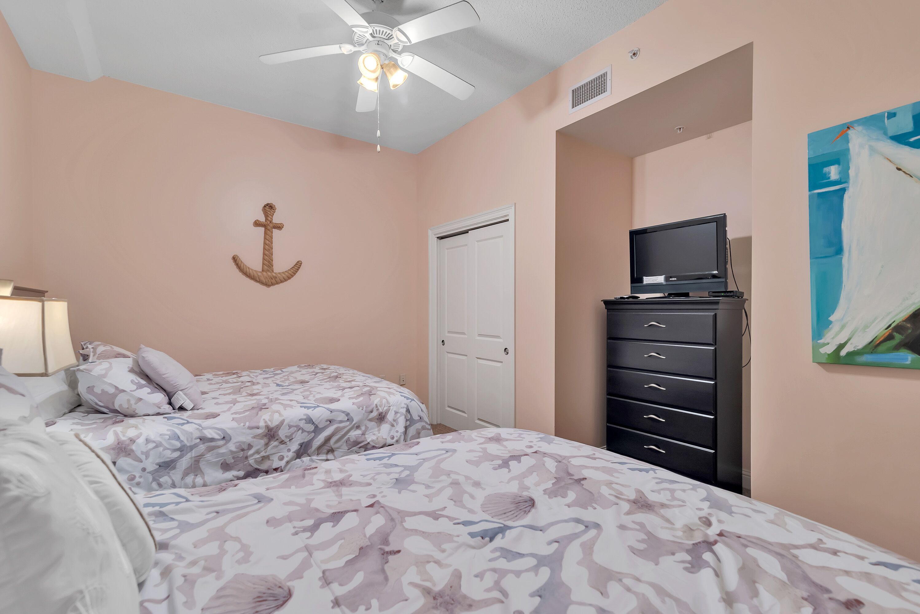 A bedroom with two beds, a ceiling fan, a TV on a dresser, and a door.