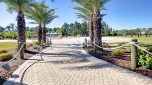 A paved pathway lined with palm trees leading to a building. - The Wharf Resort 423 | Food-Shopping-Entertainment | My Beach Getaways (Orange Beach)