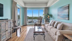 A spacious living room with a large window, a ceiling fan, a sofa, a coffee table, and a cabinet. - The Wharf Resort 423 | Food-Shopping-Entertainment | My Beach Getaways (Orange Beach)