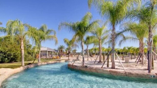 A clear pool surrounded by palm trees and a small building, likely a poolside area. - The Wharf Resort 423 | Food-Shopping-Entertainment | My Beach Getaways (Orange Beach)