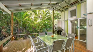 Une terrasse extérieure avec une table et des chaises en verre, un barbecue et une végétation tropicale luxuriante.
