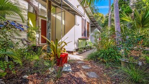 Une maison avec un chemin de jardin menant à l’entrée, entourée de différentes plantes et d’arbres.