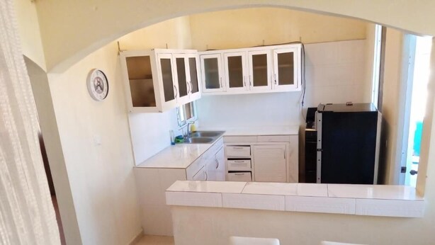 A compact kitchen with white cabinets, a black refrigerator, and a small dining area with white chairs.