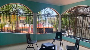 A room with a tiled floor, four chairs, a small table, and large windows with metal bars.