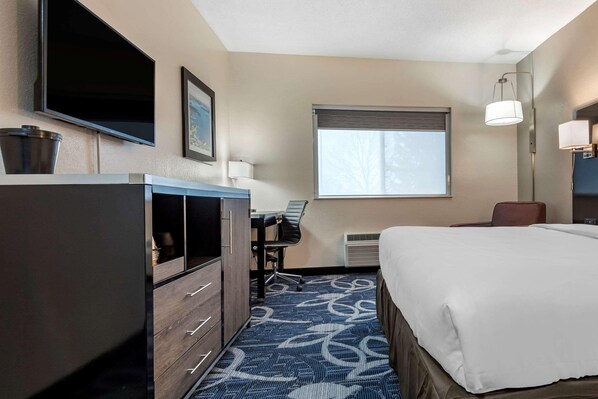A hotel room with a bed, desk, chair, TV, and window.