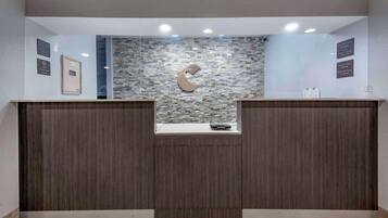 A reception desk with a stone mosaic wall, a logo, and a clock indicating check-in times.