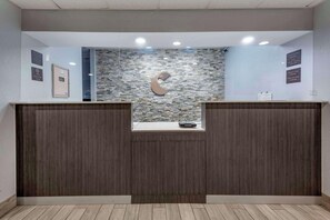 A reception desk with a stone mosaic wall, a logo, and a clock indicating check-in times.