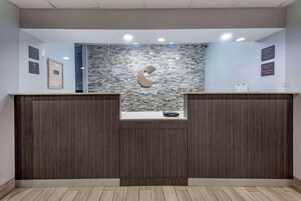 A reception desk with a stone mosaic wall, a logo, and a clock indicating check-in times.