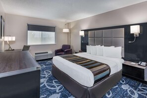 A hotel room with a large bed, a desk, a chair, a window with blinds, a wall-mounted TV, and a bedside table with a phone.