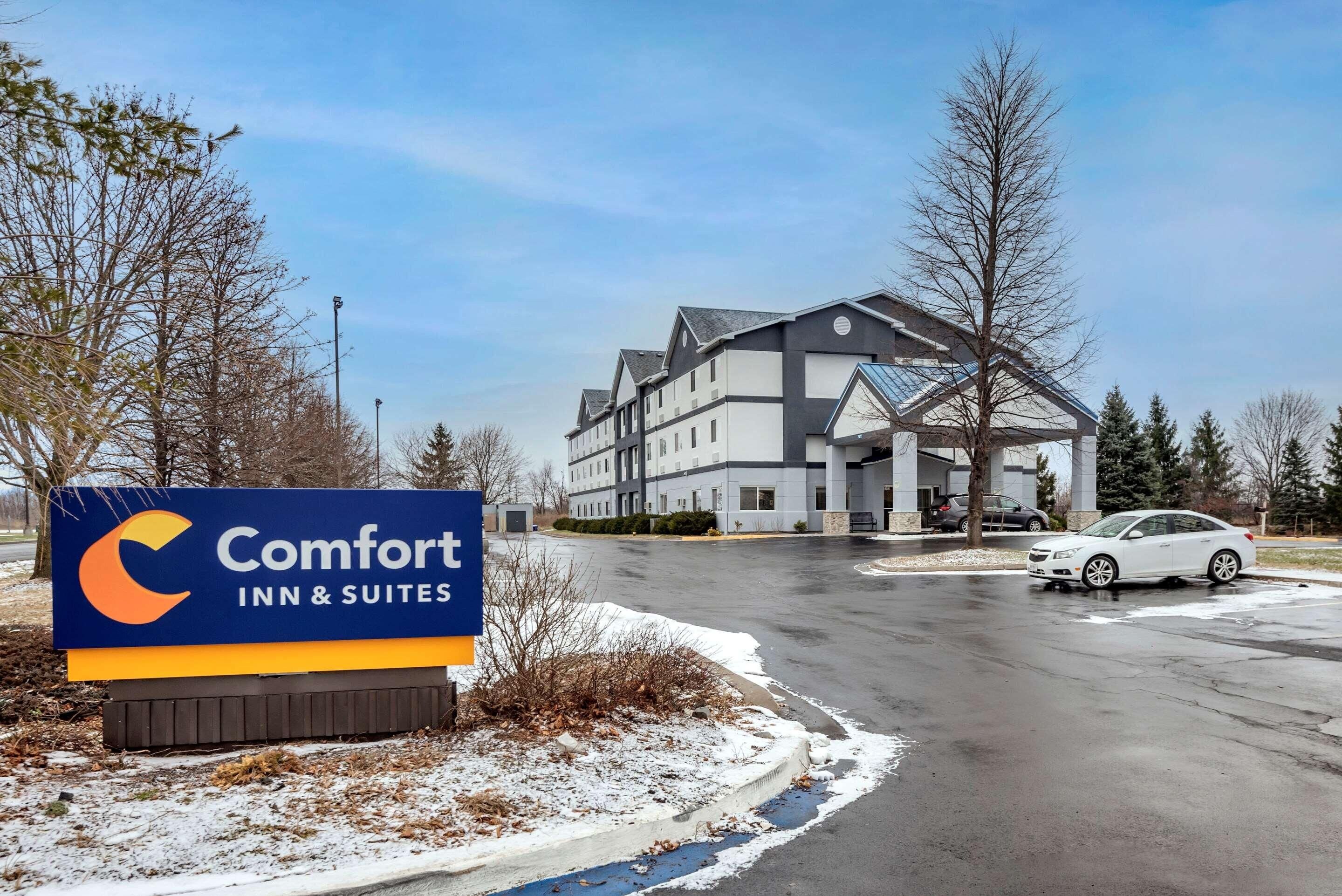 A Comfort Inn & Suites sign, a multi-story building, and a white car parked on a wet road.