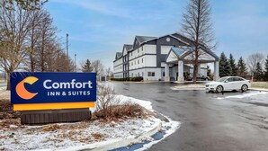 A Comfort Inn & Suites sign, a multi-story building, and a white car parked on a wet road. - Comfort Inn & Suites Liverpool - Syracuse (Liverpool)