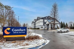 A Comfort Inn & Suites sign, a multi-story building, and a white car parked on a wet road.