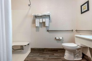 Ein Badezimmer mit Toilette, einer Duschvorhang, einem Handtuchhalter mit Handtüchern, einem Toilettenpapierhalter und einem gerahmten Bild an der Wand.