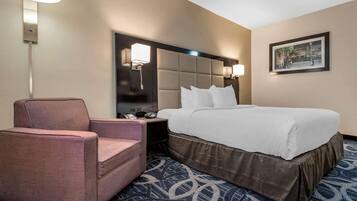 A hotel room with a bed, a chair, a nightstand, a lamp, and a framed picture on the wall.