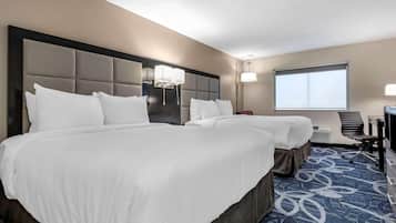 A hotel room with two beds, a desk, a chair, and a large window.