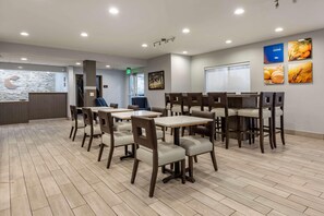 A hotel lobby with a reception desk, multiple tables and chairs, a staircase, and wall art. - Comfort Inn & Suites Liverpool - Syracuse (Liverpool)