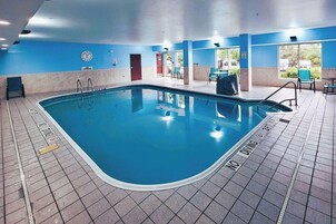 Una piscina interior con suelo de baldosas azules, un reloj en la pared y una puerta que da al exterior.