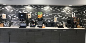 Una estación de café autoservicio con varias máquinas de café, un microondas y una vitrina de alimentos.