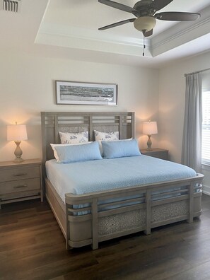Une chambre à coucher avec un lit, deux tables de chevet avec des lampes, un ventilateur de plafond et un tableau encadré au mur.