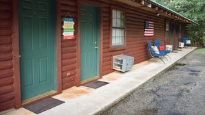 Una baita di legno con porte verdi, un piccolo portico con sedie blu e una bandiera americana.