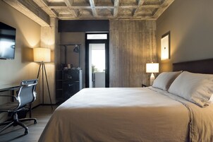 Una habitación de hotel con una cama grande, un escritorio con una silla, una lámpara de pie y un televisor montado en la pared.