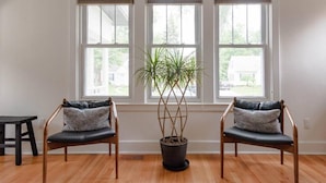 A room with three windows, a potted plant, and two chairs with cushions.
