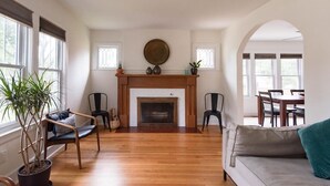 A spacious living room with a fireplace, wooden flooring, and a dining area visible through an archway.