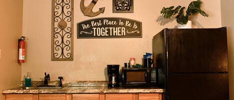 A kitchen with wooden cabinets, a black refrigerator, a coffee maker, and a fire extinguisher.