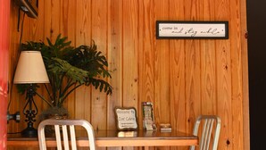 Interior de una cabaña de madera con una mesa, dos sillas, una lámpara, un letrero y una señal de bienvenida.