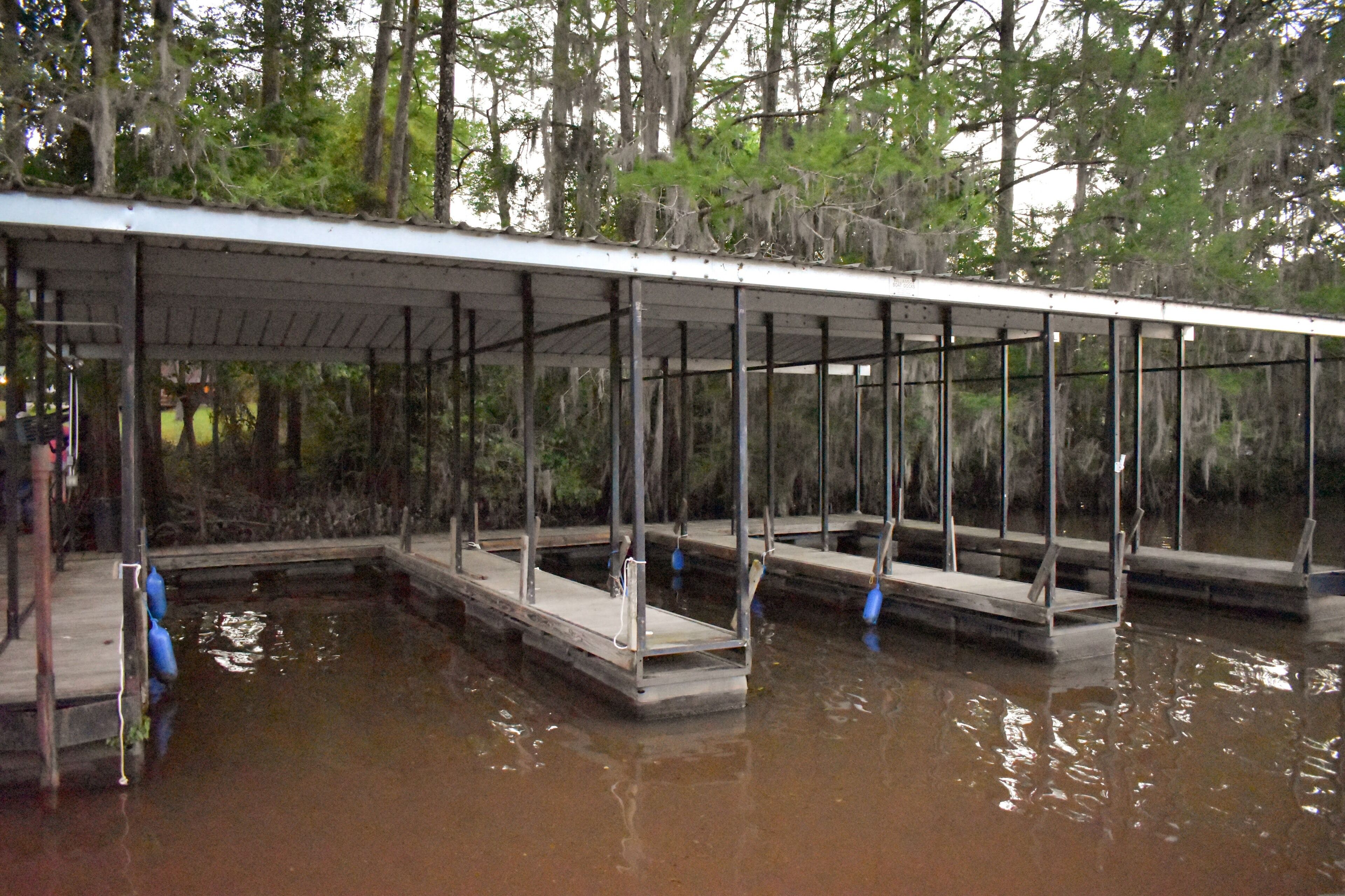 A covered dock area with multiple platforms extending into a body of water, surrounded by trees.