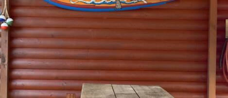 A wooden table and bench set against a red wooden wall with a sign that reads "BUMIN'THE SUN".