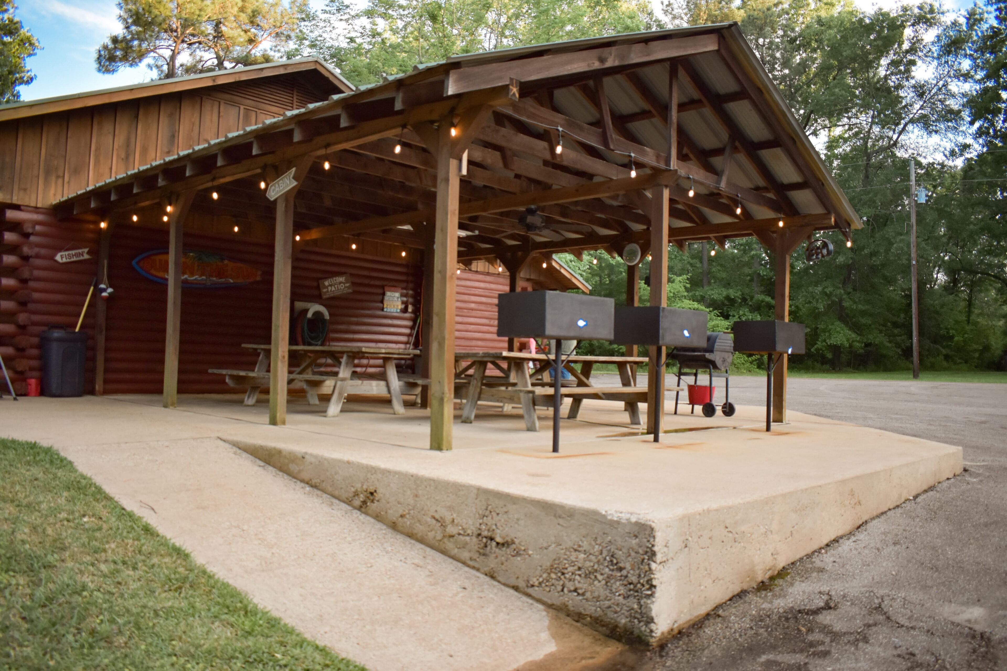 A wooden cabin with a covered picnic area, picnic tables, and barbecue grills.