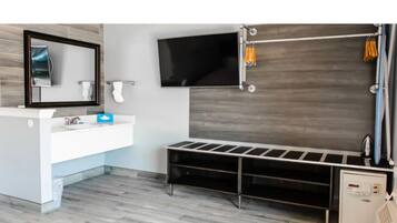 A modern bathroom with a large mirror, a flat-screen TV, a shower area, and a built-in bench.