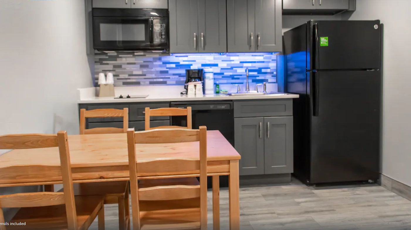A modern kitchen with grey cabinets, a black refrigerator, a microwave, and a tiled backsplash.