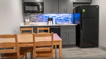 A modern kitchen with grey cabinets, a black refrigerator, a microwave, and a tiled backsplash.