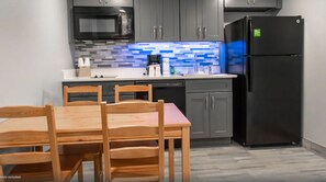 A modern kitchen with grey cabinets, a black refrigerator, a microwave, and a tiled backsplash. - Celebration Suites - 2 Miles from Disney - For 6 (Kissimmee)