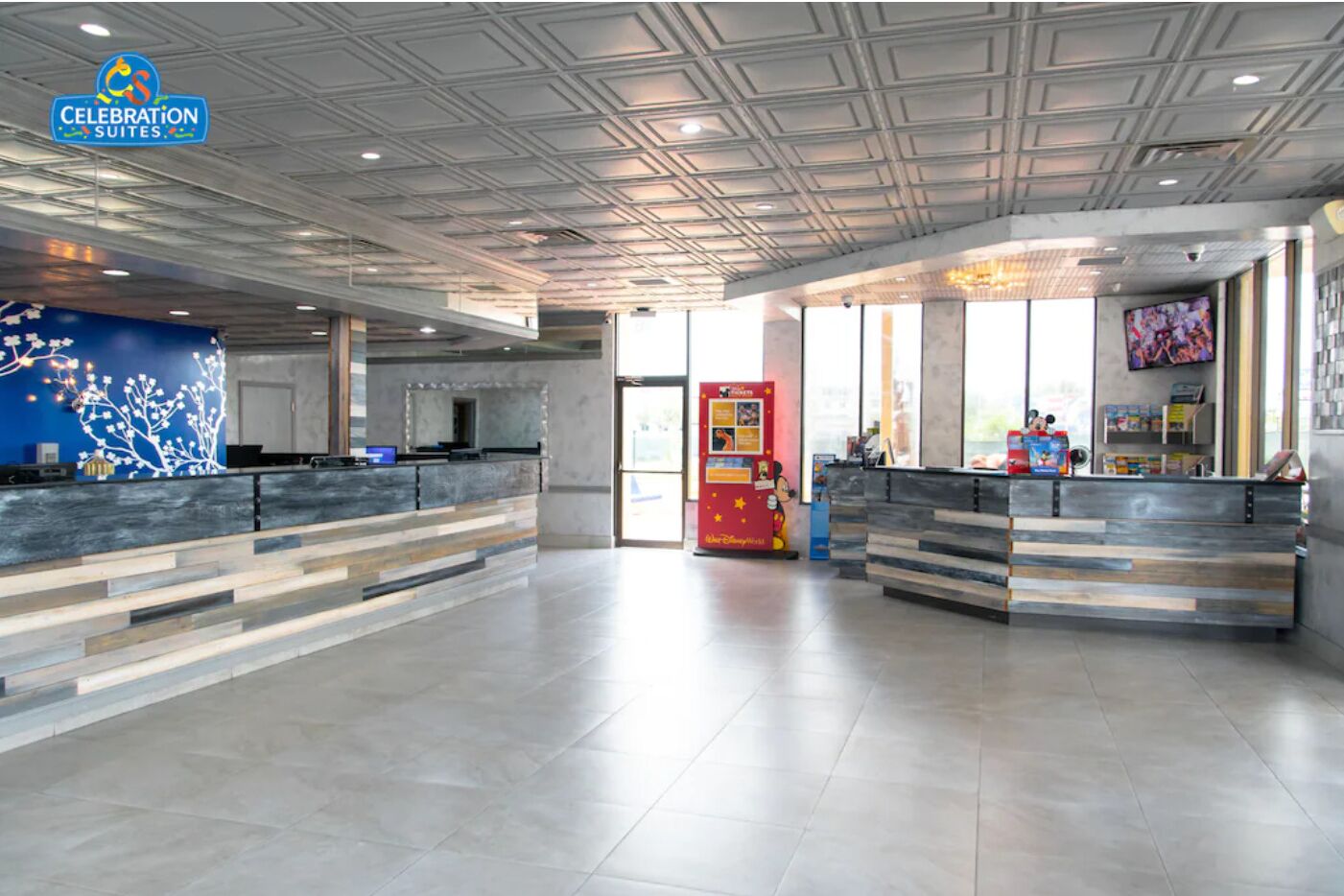 A spacious hotel lobby with two reception desks, a large window, and a ceiling with a geometric pattern.
