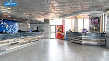 A spacious hotel lobby with two reception desks, a large window, and a ceiling with a geometric pattern.