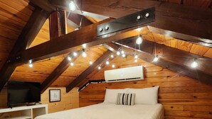 Un dormitorio acogedor en el ático con techo de madera, una cama con colcha blanca y un televisor de pared.