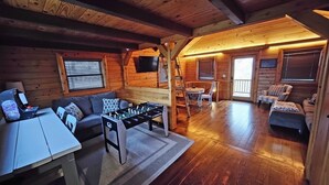 Un interior acogedor de cabaña de madera con una mesa de fútbol, sofás y un televisor montado en la pared.