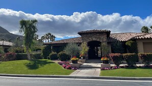A house with a stone entrance, surrounded by well-maintained lawns and colorful flower beds. - Amazing 5 bedroom Indian Wells Country Club home with private backyard! (Indian Wells)