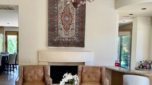 A spacious living room with a large chandelier, two leather armchairs, a coffee table with books, and a decorative rug. - Amazing 5 bedroom Indian Wells Country Club home with private backyard! (Indian Wells)