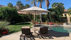 A poolside area with two wicker chairs, a table, and an umbrella. - Amazing 5 bedroom Indian Wells Country Club home with private backyard! (Indian Wells)