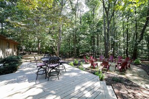 A wooden deck with outdoor furniture, surrounded by a forested area.