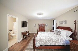A bedroom with a large bed, a wooden dresser, a desk, a television, and a wardrobe.
