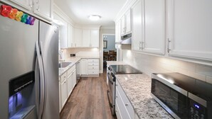 A modern kitchen with white cabinets, stainless steel appliances, and a wooden floor.