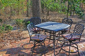 A metal table and chairs set on a brick patio surrounded by trees.