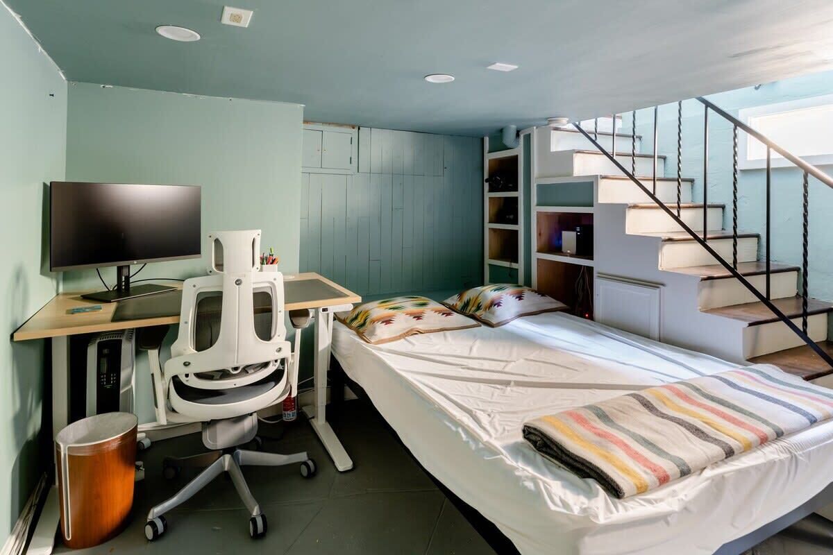 Ein gemütliches Schlafzimmer mit Bett, Schreibtisch, Computer, Stuhl und Bücherregal.